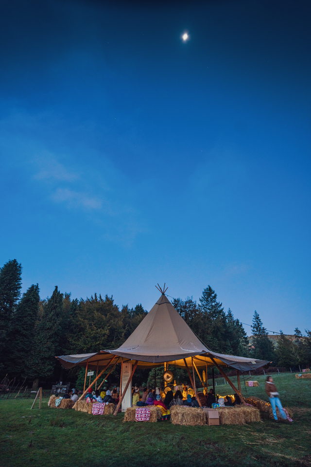Tenda tipi iluminada por dentro ao anoitecer, com a lua no céu